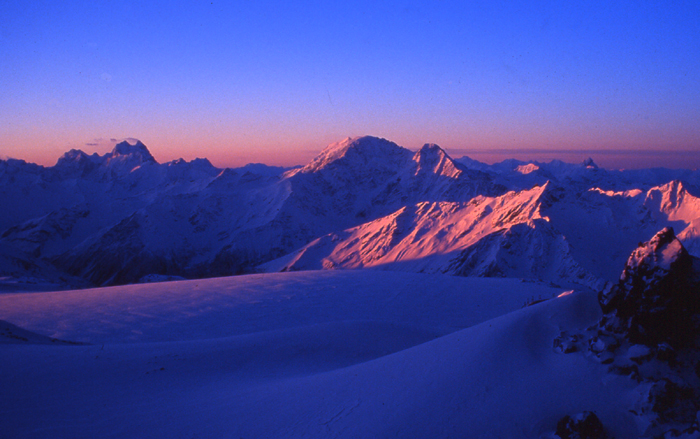 Sunrise over the central Caucasus. 
  Ushba is the peak in the distance on the left. The nearer peaks are Dongusoron and Nakra.